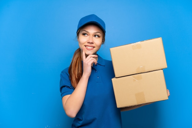 Entregadora na parede azul isolada pensando uma ideia enquanto olha para cima