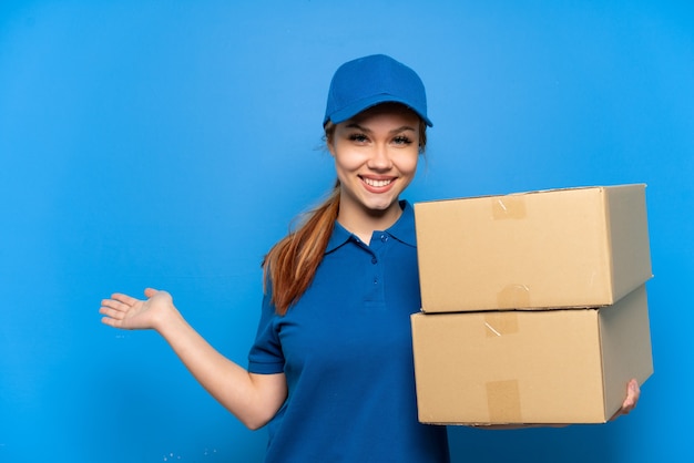 Entregadora sobre parede azul isolada estendendo as mãos para o lado para convidar para vir