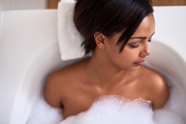 Entregando-se a um banho feliz Foto de uma jovem atraente relaxando em um banho de espuma