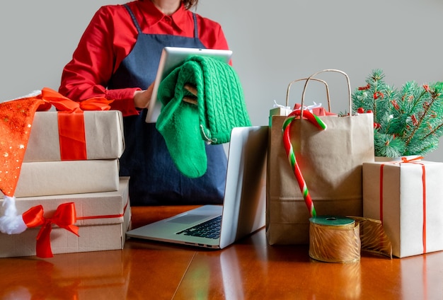 Entregar las manos usando la tableta cerca con el portátil, la bolsa de embalaje, las cajas de regalo y el árbol de Navidad. Concepto de entrega en línea.