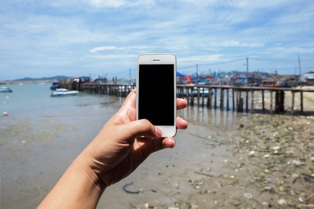 Entregue a posse o telefone móvel branco com o mar e porto frescos bonitos.