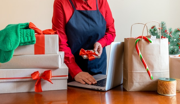 Entregue as mãos usando um laptop perto de Saco de embalagem, Caixas de presente e Árvore de Natal. Conceito de entrega online.