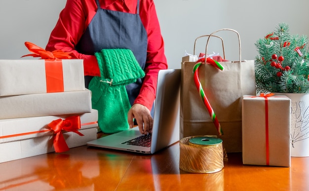Entregue as mãos usando um laptop perto de Saco de embalagem, Caixas de presente e Árvore de Natal. Conceito de entrega online.