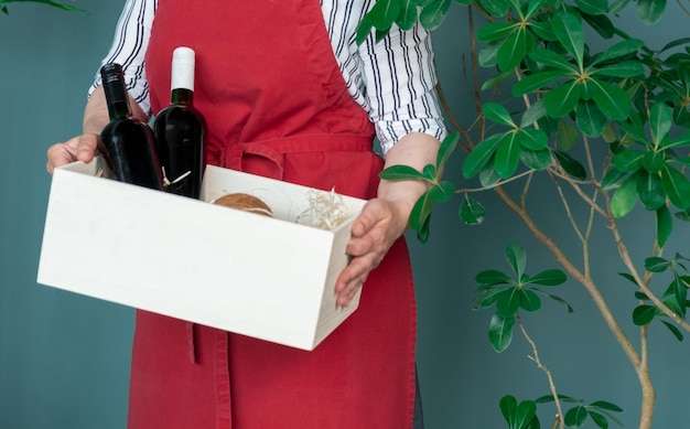 Entregue em um avental vermelho Armazena garrafas de vinho em uma caixa branca com cocos e abacate, conceito de pedido online.