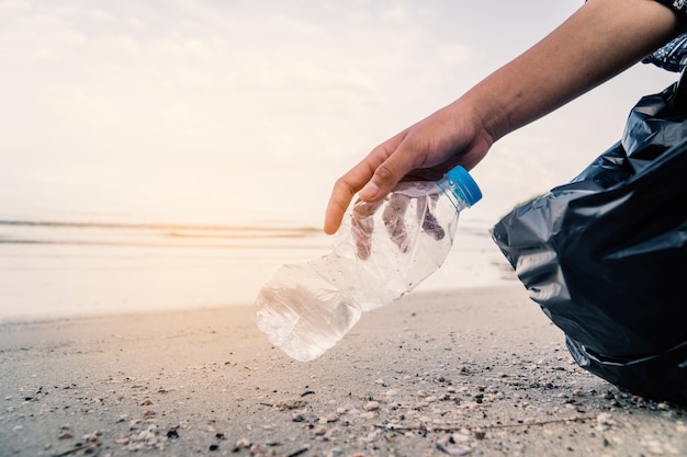 Entregue pegar a limpeza de garrafa plástica na praia, conceito voluntário.