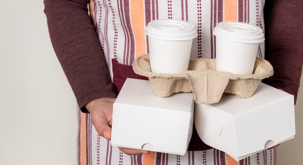 Foto entregue segurando caixas de papel e recipiente leve com duas xícaras de café branco.