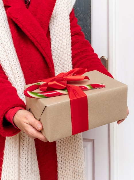 Entregue vestido com um casaco vermelho segurando Caixas de presente perto da porta branca na véspera das festas de Natal