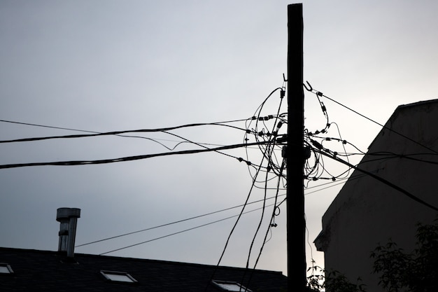 Entrelazado de cables eléctricos en una gran ciudad contra el cielo. Silueta de un pilar