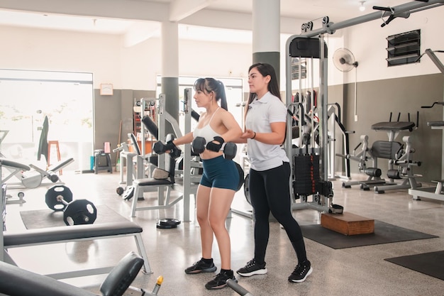 Entrenador ayudando a una chica de fitness a realizar un vuelo lateral con pesas en el gimnasio