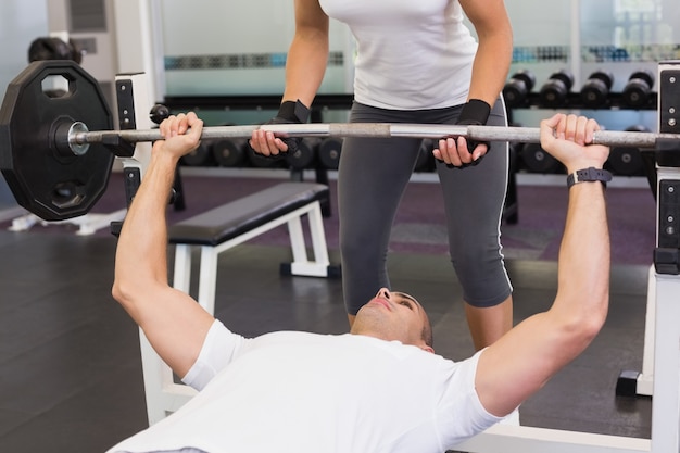 Entrenador ayudando a hombre con levantamiento de pesas en el gimnasio