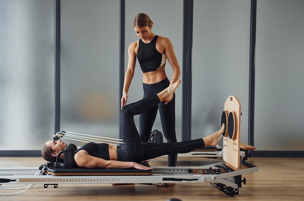 Entrenador ayudando a niña Dos mujeres en ropa deportiva y con cuerpos delgados tienen un día de yoga fitness juntos en el interior