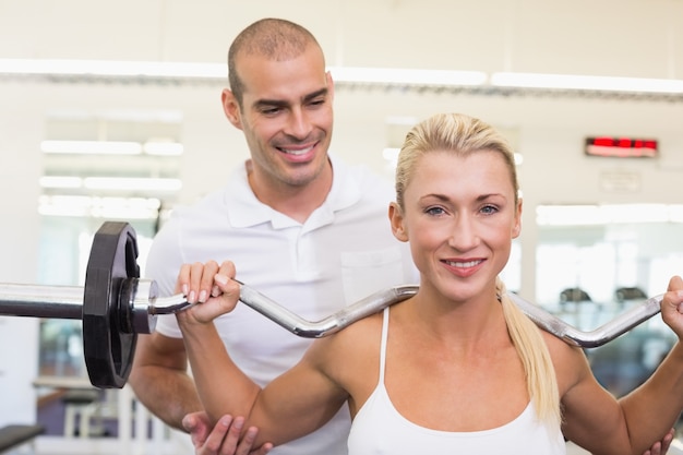 Entrenador de ayudar a la mujer con levantamiento de pesas en el gimnasio