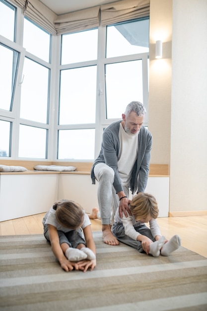 Entrenador de casa. Padre entrenando a sus hijos en casa haciéndolos estirar correctamente