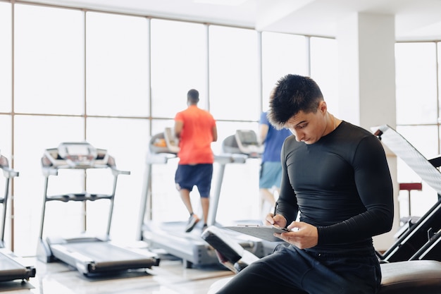 Entrenador chico joven toma notas en el gimnasio. entrenador personal para deportes.