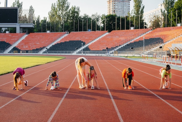 Un entrenador enseña a un gran grupo de chicas al principio antes de correr en el estadio durante la puesta de sol Un estilo de vida saludable