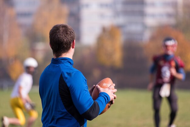 Entrenador del equipo lanzando la pelota al grupo de jóvenes jugadores de fútbol americano en acción durante el entrenamiento en el campo