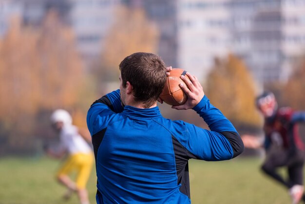 Entrenador del equipo lanzando la pelota al grupo de jóvenes jugadores de fútbol americano en acción durante el entrenamiento en el campo