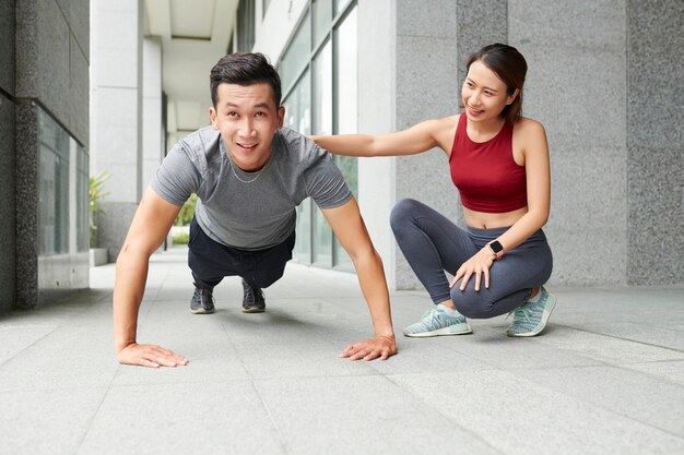 Entrenador femenino control de ajuste joven haciendo flexiones al aire libre