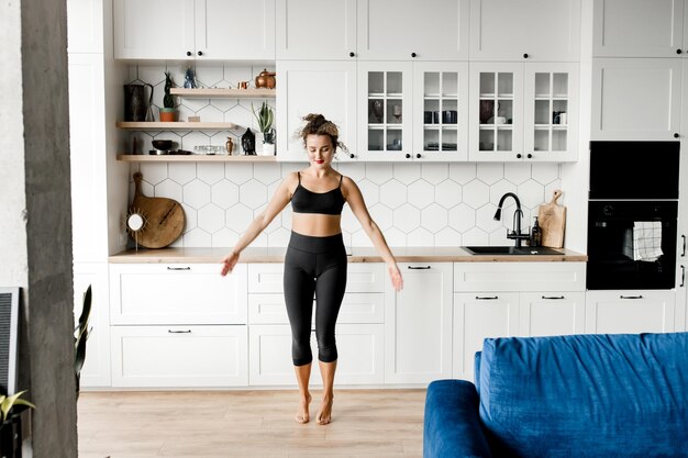 Foto entrenador de fitness de chica deportiva muestra lecciones en línea joven chica rizada sana haciendo yoga en casa mientras