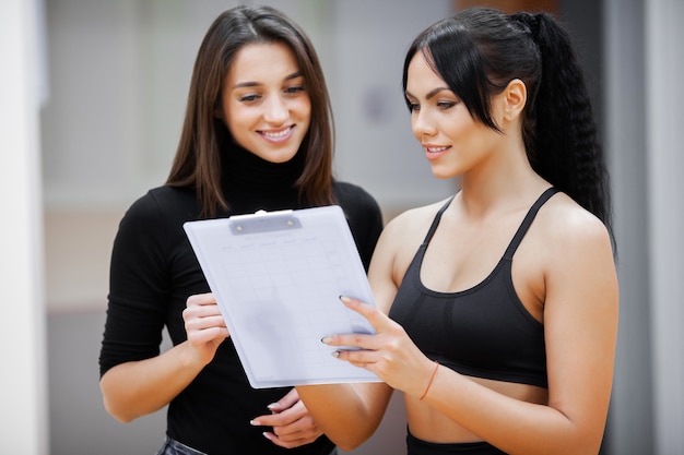 Entrenador de fitness femenino escribe un programa de entrenamiento para el gimnasio del cliente