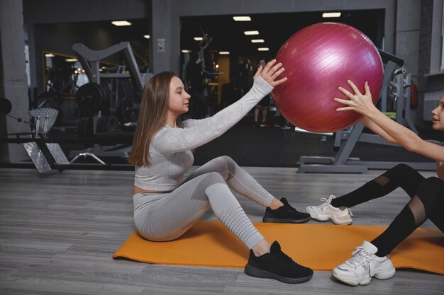 Entrenador de fitness haciendo ejercicio con su cliente adolescente haciendo sentadillas de pelota en forma