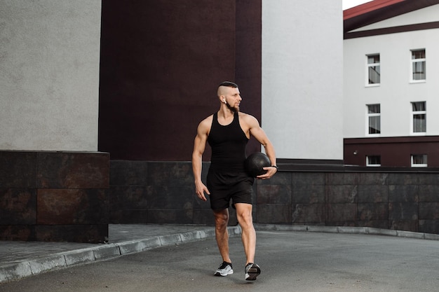 Entrenador de fitness muscular está caminando con un fitball pesado al aire libre