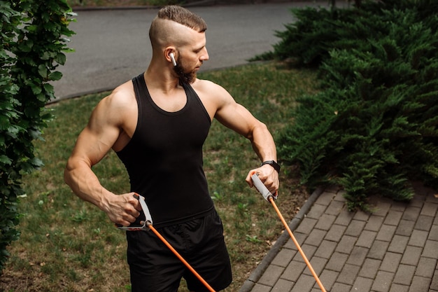 Entrenador de fitness muscular haciendo ejercicios con goma elástica al aire libre