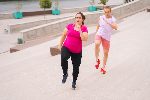 Entrenador de fitness personal ayudando a la mujer gorda a perder peso fuera corriendo en las escaleras de la ciudad en