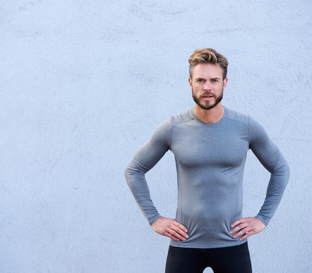 Entrenador de fitness serio de pie contra el fondo gris