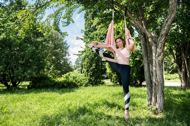 El entrenador de fly yoga se dedica a estirarse en una hamaca de aire unida a un árbol