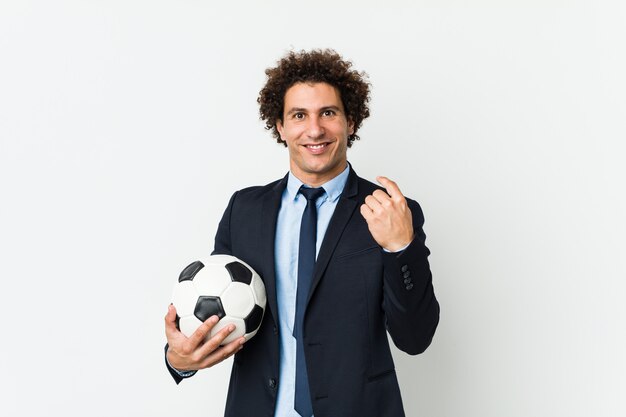 Foto entrenador de fútbol sosteniendo una pelota apuntando con el dedo hacia usted como si invitara a acercarse.