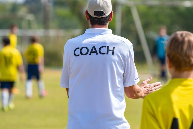 Entrenador de fútbol vistiendo una camiseta blanca de COACH en un campo de deportes al aire libre entrenando a su equipo