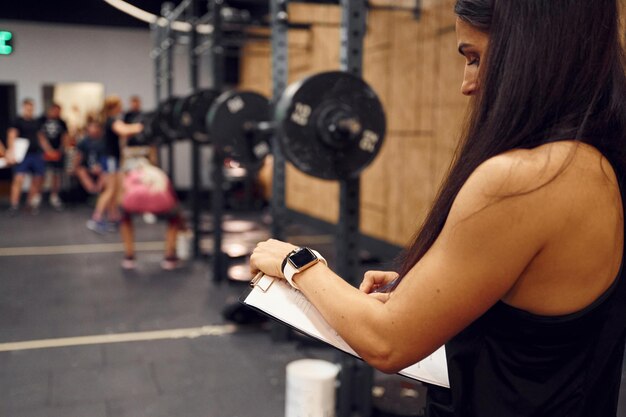 Foto entrenador de gimnasio profesional está de pie en el interior con el bloc de notas en las manos