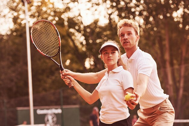 Entrenador de juego de tenis de estudiante de enseñanza en la cancha al aire libre.