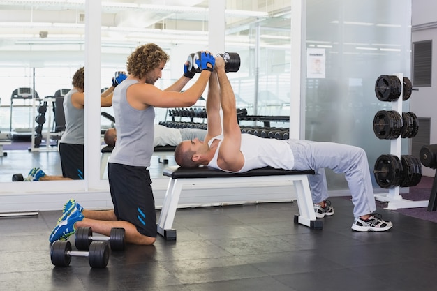 Entrenador masculino ayudando a hombre joven con pesas en el gimnasio