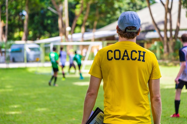 Entrenador masculino de fútbol o fútbol parado en la línea lateral viendo a su equipo jugar