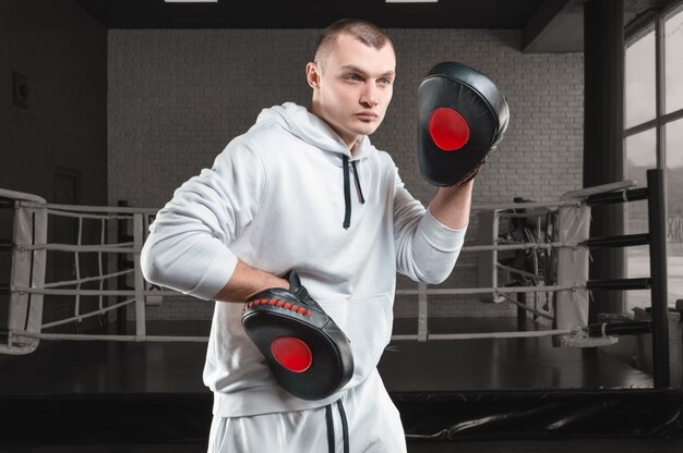 Entrenador masculino en el gimnasio contra el ring tiene patas de boxeo. Concepto de artes marciales mixtas.