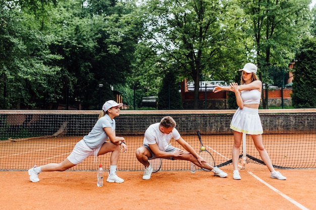 Entrenador masculino tenista y dos mujeres estira antes de jugar. Equipo joven junto.