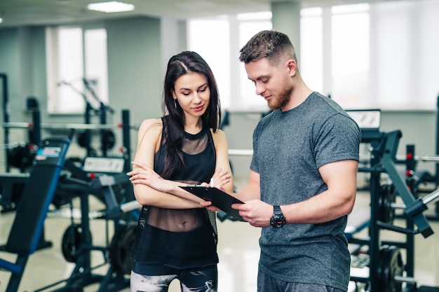 El entrenador muscular muestra los resultados deportivos de la mujer en el gimnasio