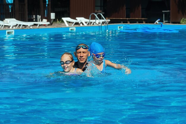 Entrenador de natación dando una lección con dos niñas en la piscina al aire libre de agua azul en un día cálido y soleado