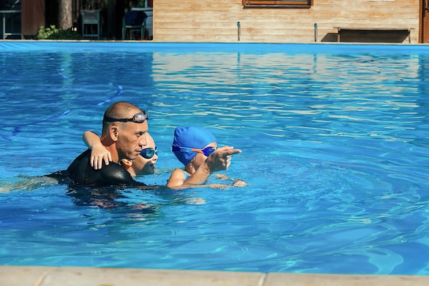 Entrenador de natación dando lecciones a dos niñas en la piscina al aire libre con agua azul