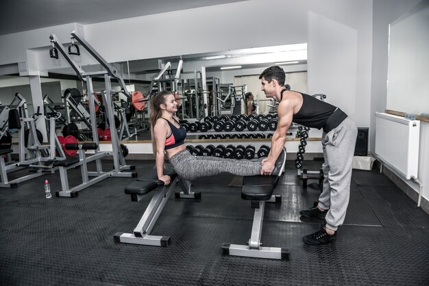 Entrenador personal ayudando a la mujer joven en el gimnasio