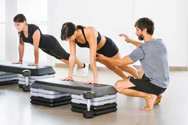 Entrenador personal masculino joven que ayuda a una mujer que hace una pose de tabla de yoga en una clase en un gimnasio espacioso y luminoso en un concepto de salud y fitness o estilo de vida saludable