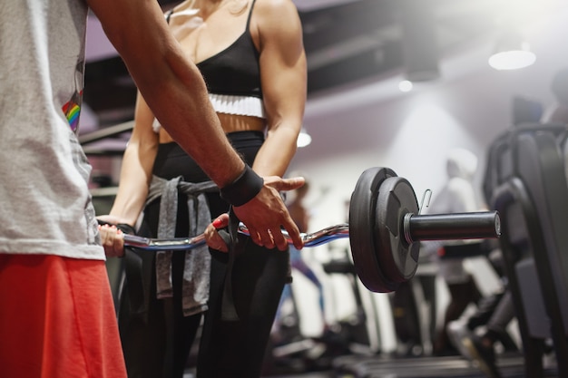 El entrenador personal muestra a una joven la correcta implementación de ejercicios con una barra durante un entrenamiento en el gimnasio.