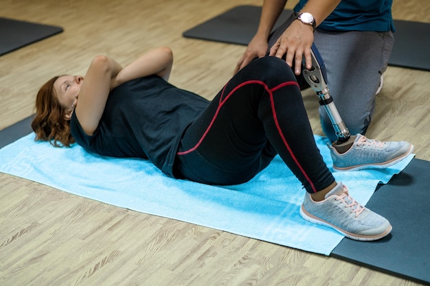 Entrenador personal que ayuda a una mujer con discapacidad en su entrenamiento. Centro de Rehabilitación Deportiva con fisioterapeutas y pacientes trabajando juntos hacia la curación.