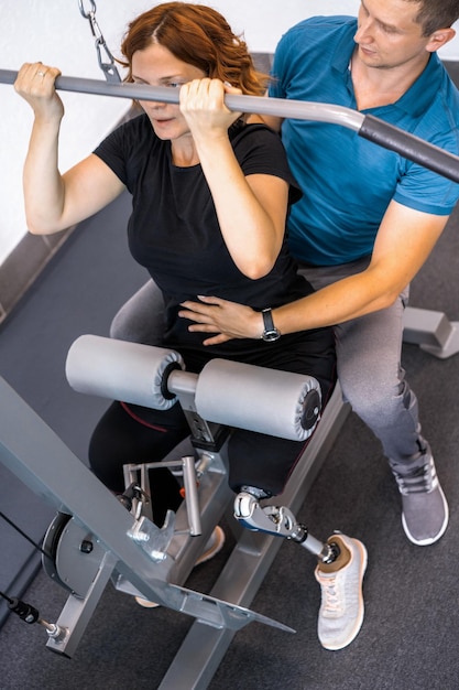 Entrenador personal que ayuda a una mujer con discapacidad en su entrenamiento. Centro de Rehabilitación Deportiva con fisioterapeutas y pacientes trabajando juntos hacia la curación.