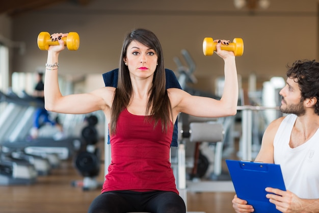 Entrenador personal que mira a una mujer de entrenamiento en el gimnasio