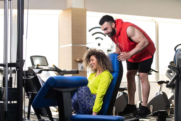 Entrenador personal que muestra a una mujer joven cómo entrenar piernas en una máquina en el gimnasio