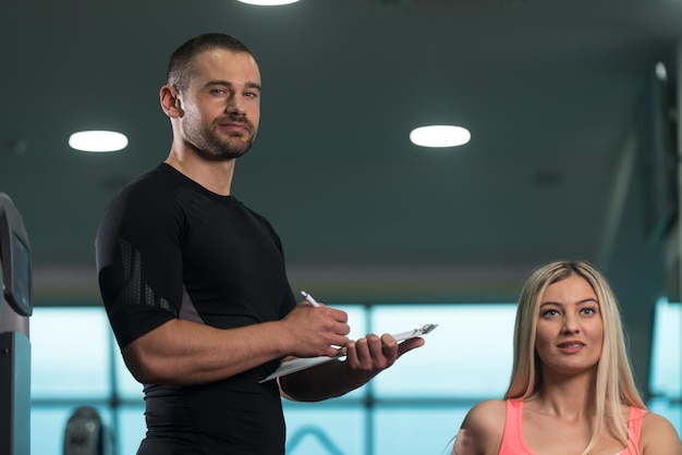 Entrenador personal que muestra a la mujer joven cómo volver a entrenar en la máquina en el gimnasio