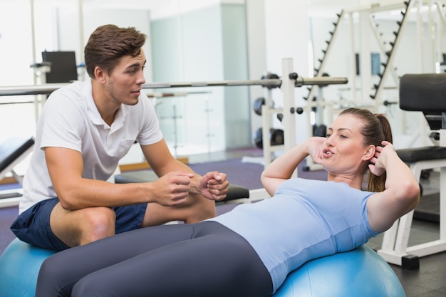 Entrenador personal que trabaja con el cliente en la bola del ejercicio en el gimnasio